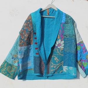 May include: A turquoise blue quilted jacket with a patchwork design featuring various floral and geometric patterns. The jacket has a shawl collar and long sleeves.