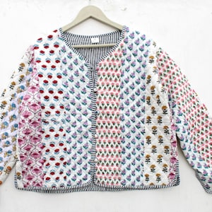 May include: A quilted jacket with a floral pattern in red, pink, yellow, and purple on a white background. The jacket has a black and white striped lining and trim. The jacket is hanging on a wooden hanger.
