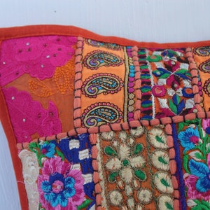 Puede incluir: Una funda de coj&iacute;n de patchwork colorido con bordados intrincados en tonos de rosa, naranja, azul y verde. La funda est&aacute; hecha de varias telas cosidas juntas en un patr&oacute;n cuadrado.