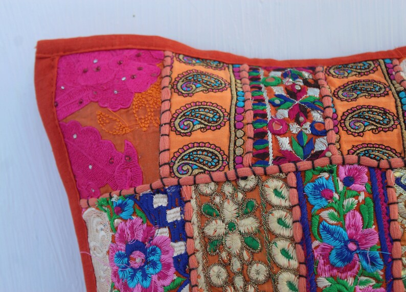 Puede incluir: Una funda de coj&iacute;n de patchwork colorido con bordados intrincados en tonos de rosa, naranja, azul y verde. La funda est&aacute; hecha de varias telas cosidas juntas en un patr&oacute;n cuadrado.
