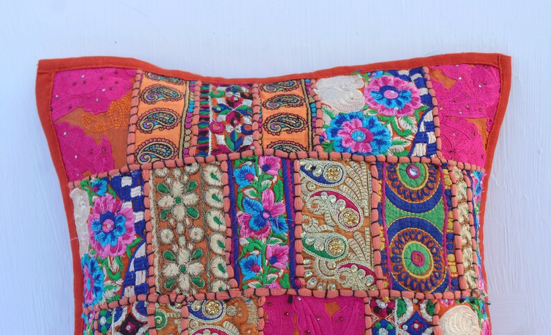 Puede incluir: Una almohada de patchwork colorida con bordados florales y lentejuelas. La almohada est&aacute; hecha de varias telas en tonos de rosa, naranja, azul, verde y dorado.