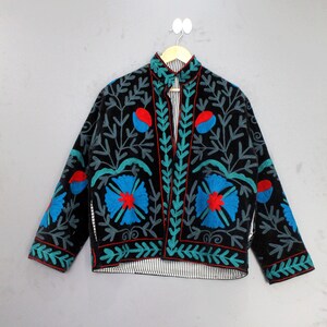 Puede incluir: Chaqueta negra con bordados florales en azul, rojo y turquesa. La chaqueta tiene cuello mandarín y forro a rayas. El bordado presenta flores estilizadas y patrones de hojas, creando un diseño único y artístico.