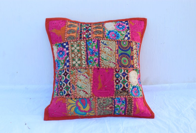 Puede incluir: Una funda de coj&iacute;n de patchwork colorido con fondo rosa y bordados intrincados. La funda est&aacute; hecha de varias telas y presenta una variedad de colores, incluyendo naranja, azul, verde y amarillo.