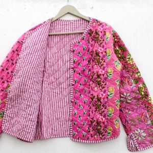 Può includere: Una giacca trapuntata rosa e bianca con una stampa floreale su un lato e un motivo a righe sull'altro. La giacca ha un collo a V e maniche lunghe.