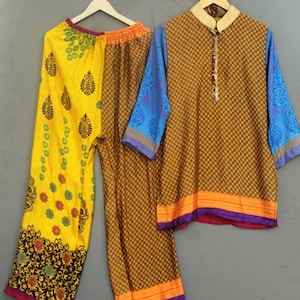 Könnte beinhalten: Ein zweiteiliges Set bestehend aus einer Hose mit weitem Bein und einer langärmeligen Tunika. Die Hose hat ein gelbes Paneel mit dunklen Blumenmotiven und ein braunes Paneel mit geometrischem Muster. Die Tunika hat einen braunen Druck.