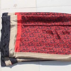Könnte beinhalten: Gefalteter Stoff mit rotem und schwarzem Muster und goldenem Rand. Der Stoff hat ein sich wiederholendes Blumenmuster in Schwarz auf rotem Hintergrund. Der Rand ist goldfarben mit einem strukturierten Muster. Der Stoff ist sauber gefaltet.