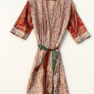 Pode incluir: Uma bata de seda branca com estampa floral e mangas com padrão vermelho e dourado. A bata tem uma faixa verde e marrom.