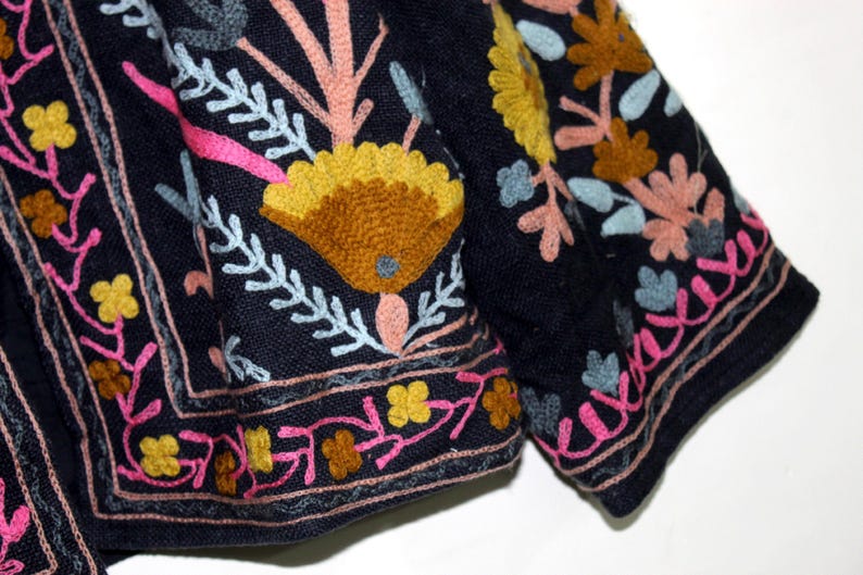 Pu&ograve; includere: Primo piano di un tessuto blu scuro con ricami floreali colorati. Il ricamo presenta fiori gialli, rosa e arancioni, con accenti azzurri e bianchi. Il design &egrave; intricato e dettagliato, con un bordo.