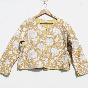 Könnte beinhalten: Eine gesteppte Jacke mit gelbem und weißem Blumendruck und Knopfverschluss. Die Jacke hat lange Ärmel und eine verkürzte Länge.