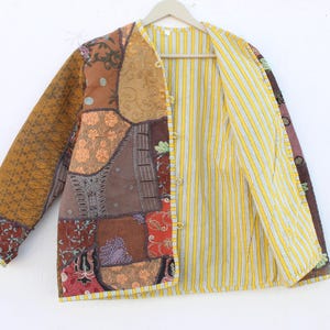 Può includere: Una giacca a patchwork con una fodera a righe gialle e bianche. La giacca è realizzata con diversi tessuti e colori, tra cui marrone, arancione, rosso e verde. La giacca ha una chiusura con bottone e maniche lunghe.