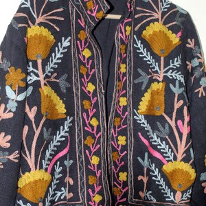 Pu&ograve; includere: Giacca blu navy scuro con ricami floreali colorati. La giacca presenta grandi fiori stilizzati in tonalit&agrave; oro e giallo, con accenti rosa, blu e verdi. Il ricamo &egrave; dettagliato e copre la parte anteriore, il colletto e le maniche.