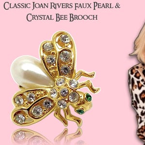 May include: A gold-coloured bee brooch with faux pearl and crystal detailing. The brooch has a large faux pearl and is decorated with many clear crystals. The text "CLASSIC JOAN RIVERS FAUX PEARL & CRYSTAL BEE BROOCH" is at the top.