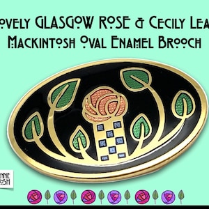 May include: Oval enamel brooch with a black background and gold trim. The brooch features a rose and leaf design in green, orange, and blue, with the text "LOVELY GLASGOW ROSE & CECILY LEAF MACKINTOSH OVAL ENAMEL BROOCH".