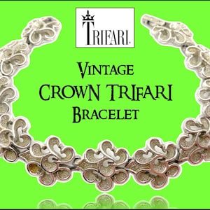 Può includere: Un braccialetto Trifari vintage a corona con un design floreale. Il braccialetto in metallo argentato è esposto su uno sfondo verde brillante. È visibile anche il testo "Vintage Crown Trifari Bracelet".