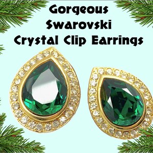 May include: A pair of clip-on earrings featuring a teardrop-shaped emerald green crystal surrounded by a halo of clear rhinestones. The earrings have a gold-tone setting.