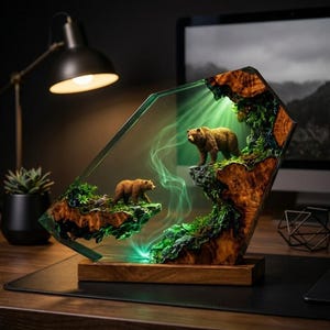 May include: A decorative lamp featuring two brown bear figurines placed on natural wood and green foliage elements encased in a clear, angular resin frame. The piece is illuminated from within, casting a soft green glow and light smoke effects.