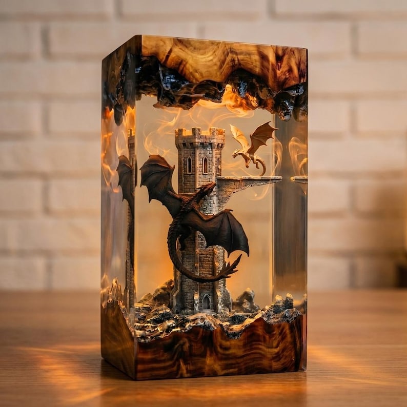 Pu&ograve; includere: Una lampada rettangolare in resina con base e parte superiore in legno naturale. All'interno della resina trasparente, una torre color pietra poggia su una base rocciosa. Un grande drago nero avvolge la torre, mentre un drago dorato vola.