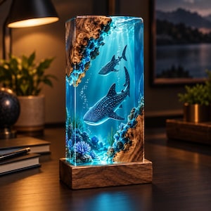 May include: A rectangular resin lamp featuring two whale sharks swimming in a deep blue underwater scene. The piece incorporates natural wood elements at the top and bottom, with blue coral and bubbles illuminated within the clear resin block.