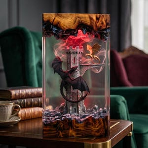 Pu&ograve; includere: Una lampada rettangolare in resina con base e parte superiore in legno naturale. All'interno, una torre color pietra si erge tra effetti di luce rossa vorticosi. Un drago rosso scuro si aggrappa alla torre, mentre un drago dorato pi&ugrave; piccolo &egrave; appollaiato.