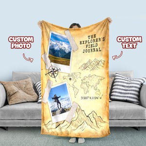Puede incluir: Una manta beige con un diseño de mapa, brújula e ilustraciones de montañas. La manta presenta dos marcos de fotos con imágenes de montañas y personas, y el texto "THE EXPLORER'S FIELD JOURNAL".