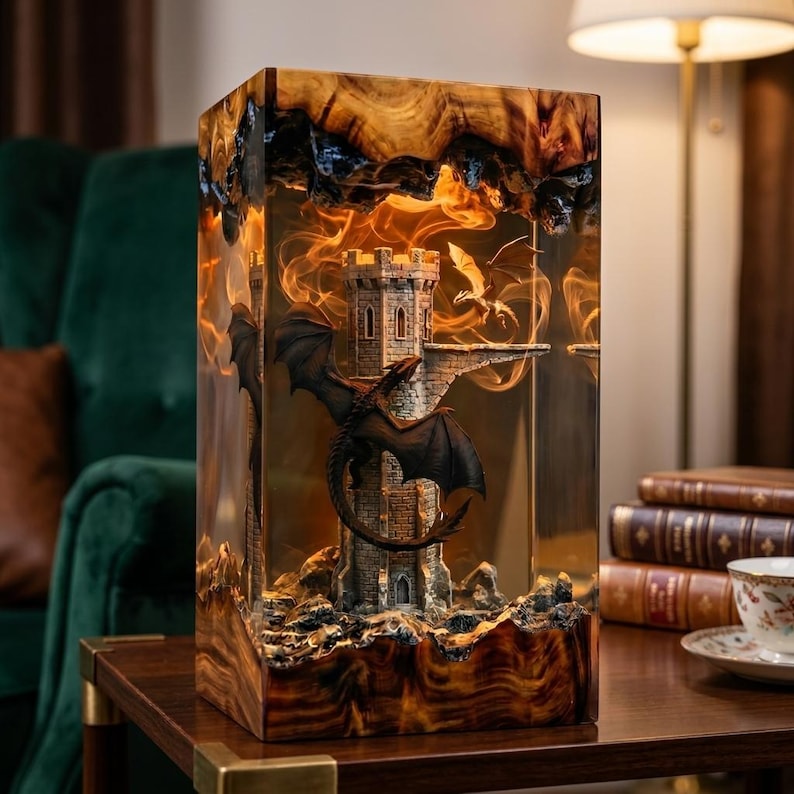 Pu&ograve; includere: Una lampada rettangolare in resina e legno con una scultura interna a forma di torre in pietra, un drago scuro appollaiato sul lato e un drago pi&ugrave; piccolo che vola sopra, il tutto illuminato da una calda luce arancione.