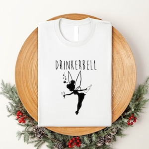 May include: White t-shirt with a black silhouette of a fairy holding a glass of wine and a bottle of wine. The text "DRINKERBELL" is above the fairy.