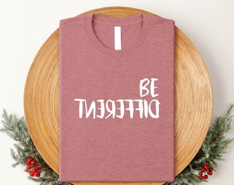 Könnte beinhalten: Ein mauvefarbenes T-Shirt mit dem Aufdruck "BE DIFFERENT" in Weiß auf der Vorderseite.