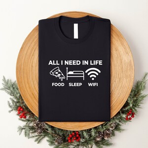May include: Black t-shirt with white text that reads "All I need in life: Food, Sleep, Wifi". The text is accompanied by icons of a pizza slice, a bed, and a wifi symbol.