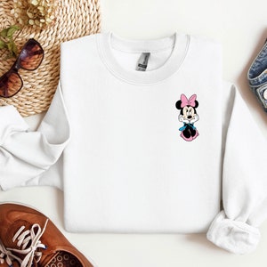 Peut inclure: Sweat-shirt blanc &agrave; col rond avec une image de dessin anim&eacute; de Minnie Mouse portant un n&oelig;ud rose et une robe bleue.