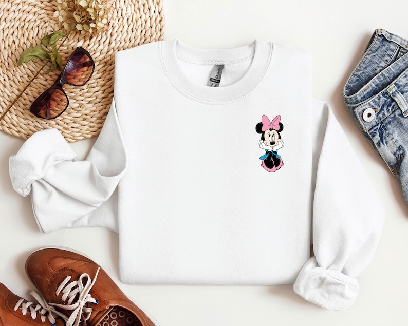 Peut inclure: Sweat-shirt blanc &agrave; col rond avec une image de dessin anim&eacute; de Minnie Mouse portant un n&oelig;ud rose et une robe bleue.