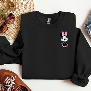 Peut inclure: Sweat-shirt noir avec un petit graphique de Minnie Mouse portant un n&oelig;ud rose et une robe bleue.