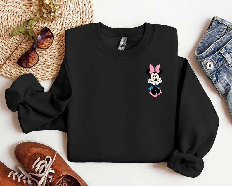 Peut inclure: Sweat-shirt noir avec un petit graphique de Minnie Mouse portant un n&oelig;ud rose et une robe bleue.