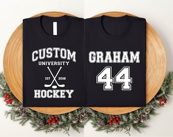 May include: Two black t-shirts with white text. The first shirt says "Custom University Est. 2018 Hockey" with a pair of crossed hockey sticks. The second shirt says "Graham 44".