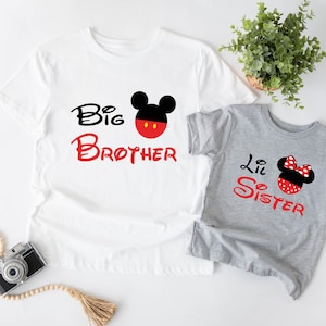 以下が含まれることがあります： ミッキーマウスとミニーマウスのデザインが施された白いTシャツ2枚。大きい方のTシャツには「お兄ちゃん」と書いてあり、小さい方のTシャツには「妹」と書いてあります。