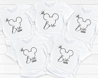 Könnte beinhalten: Fünf weiße T-Shirts mit einem schwarzen Mickey-Maus-Kopfdesign und dem Text "Bride Squad" auf jedem Shirt.