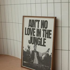 Könnte beinhalten: Ein gerahmter Schwarzweißdruck mit dem Text "Ain't no love in the jungle" und einem Foto eines DJs, der vor einer Menge auftritt.