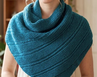 Könnte beinhalten: Ein teal-farbener Strickschal mit einem strukturierten Rippenmuster. Der Schal ist um die Schultern drapiert und bildet eine dreieckige Form. Der Strickstoff hat ein weiches Aussehen, das Wärme und Komfort suggeriert. Der Schal ist ein vielseitiges Accessoire.