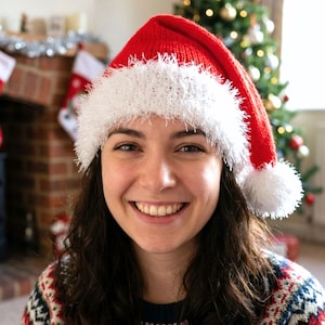 Könnte beinhalten: Eine rote Strick-Weihnachtsmütze mit einem strukturierten, flauschigen weißen Rand und einem passenden weißen Bommel an der Spitze. Die Mütze besteht aus einfarbigem rotem Garn mit einem Strickmuster und einem weichen, zotteligen weißen Saum.
