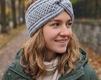 May include: A gray, hand-knitted headband with a twisted knot design. The headband is made of a textured yarn and is worn across the forehead. This winter accessory is perfect for keeping warm during cold weather.