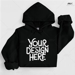 May include: Black hooded sweatshirt with the text "YOUR DESIGN HERE" in white. The hoodie has a drawstring and a kangaroo pocket. The sleeves are cuffed at the wrists. The background is plain white.