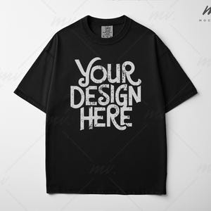 May include: Black crew neck t-shirt with the text "YOUR DESIGN HERE" in distressed white lettering. The shirt has short sleeves and a relaxed fit. The image is a product shot, likely for a clothing brand or custom design service.