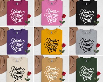 Puede incluir: Una colección de nueve camisetas de cuello redondo en varios colores, cada una con el texto "Your Design Here" en una escritura elegante. Una rosa roja se coloca cerca de cada camisa, y un sombrero marrón es visible en el fondo.
