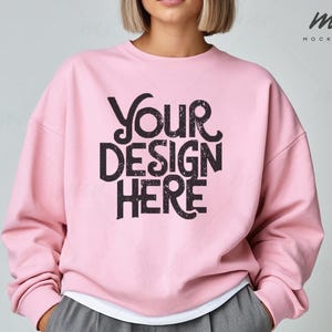 Op de afbeelding: Een roze sweatshirt met de tekst "Your Design Here" in zwarte letters. Het sweatshirt is een mockup voor een ontwerp.