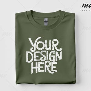 以下が含まれることがあります： 前面に白い文字で「Your Design Here」と印刷された、折り畳まれたオリーブグリーンのTシャツです。