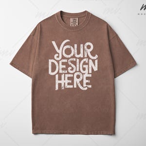 Könnte beinhalten: Ein braunes T-Shirt mit dem Text "YOUR DESIGN HERE" in weißer, verwaschener Schrift. Das kurzärmelige Shirt hat einen Rundhalsausschnitt. Das Kleidungsstück ist einfarbig und hat einen Vintage-Look.