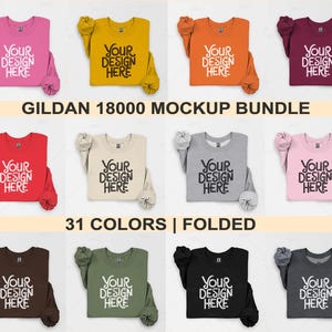 Puede incluir: Un paquete de maquetas de 31 camisetas Gildan 18000 dobladas en varios colores. Las camisetas están dobladas y dispuestas sobre un fondo blanco. El texto "YOUR DESIGN HERE" está impreso en cada camiseta.