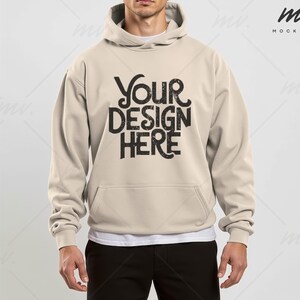 May include: A beige hoodie with a drawstring hood and a kangaroo pocket. The hoodie has the text "YOUR DESIGN HERE" printed on the front in black.