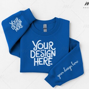 Può includere: Una felpa blu reale con la scritta "Your Design Here" in bianco sul davanti e sulle maniche. Le maniche sono piegate e la felpa è appoggiata su una superficie bianca. L'etichetta del marchio Gildan è visibile.