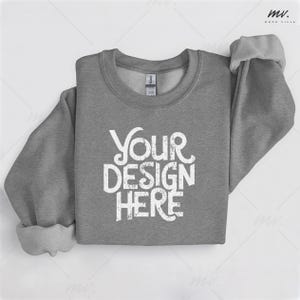 May include: A heather gray sweatshirt with the text "YOUR DESIGN HERE" in a distressed white font. The sleeves are cuffed, and the Gildan tag is visible. This apparel item is perfect for custom designs.