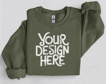 May include: An olive green crew neck sweatshirt with the text "YOUR DESIGN HERE" in distressed white lettering. The sleeves are rolled up. The sweatshirt is a Gildan brand.